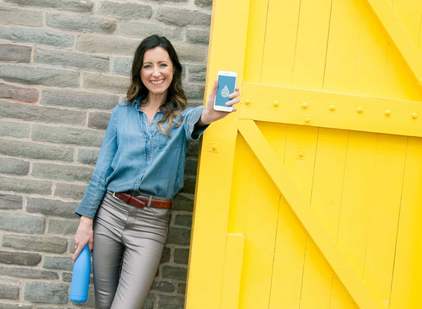 Women holding a cell phone in front of yellow door to celebrate Diags Shift app launch for job seekers